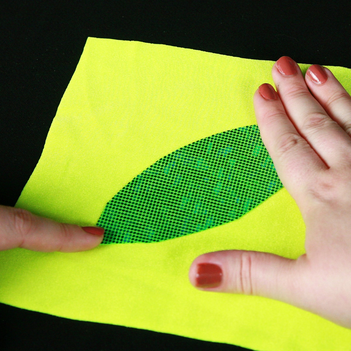 A pair of hands is smoothing out a piece of bright green spandex onto a piece of yellow spandex.