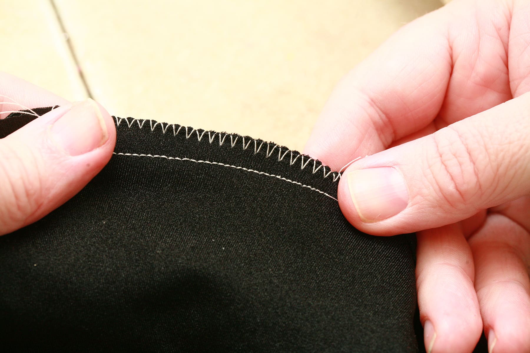 Two hands hold a piece of black spandex that has been sewn with a straight stitch and a zigzag stitch.