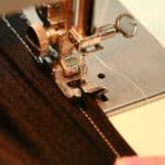 Two hands guide a piece of black spandex fabric through a sewing machine.