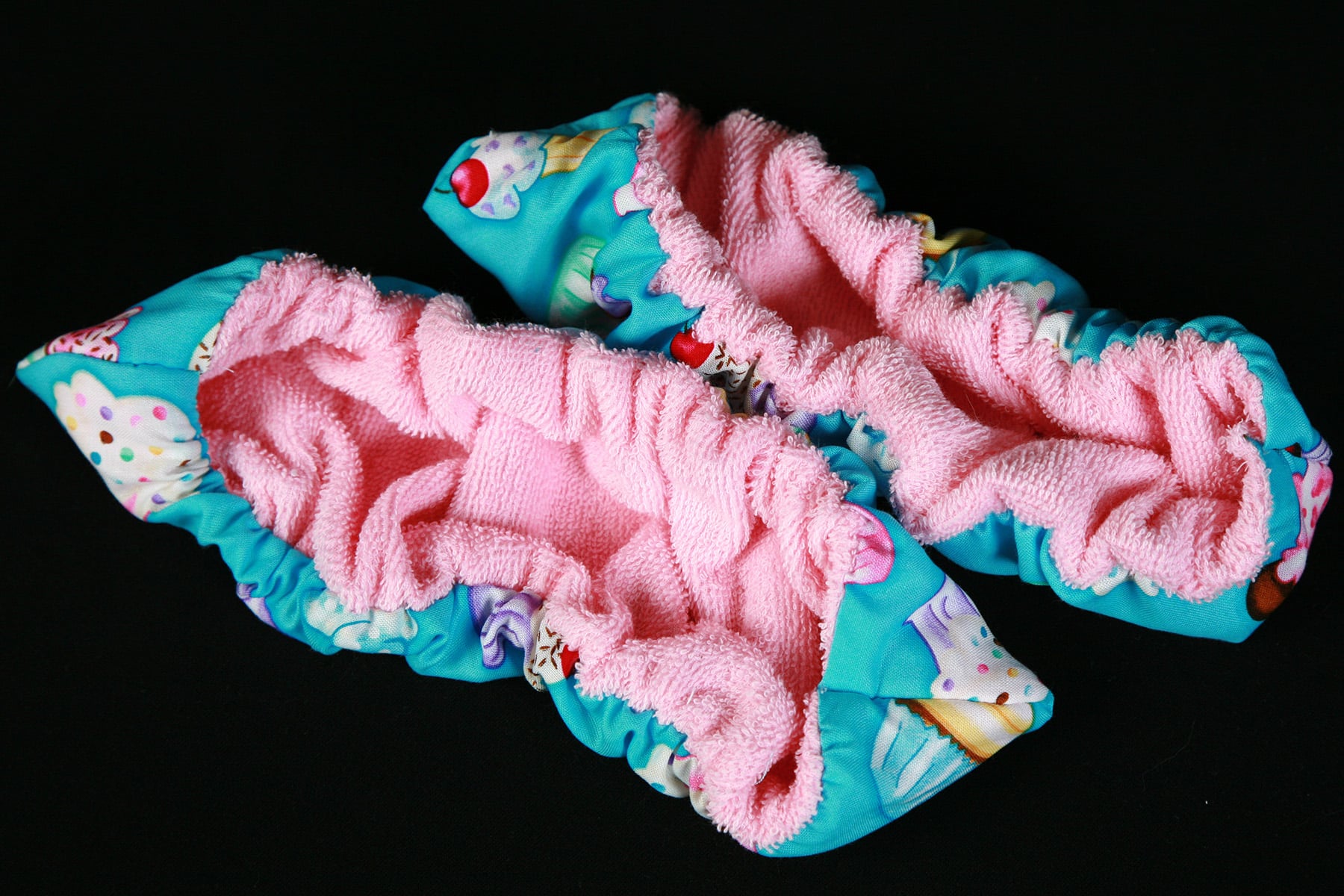 A brightly coloured pair of blade covers.  The inside is pink terrycloth, the outside is turquoise cotton with a cupcake print on it.
