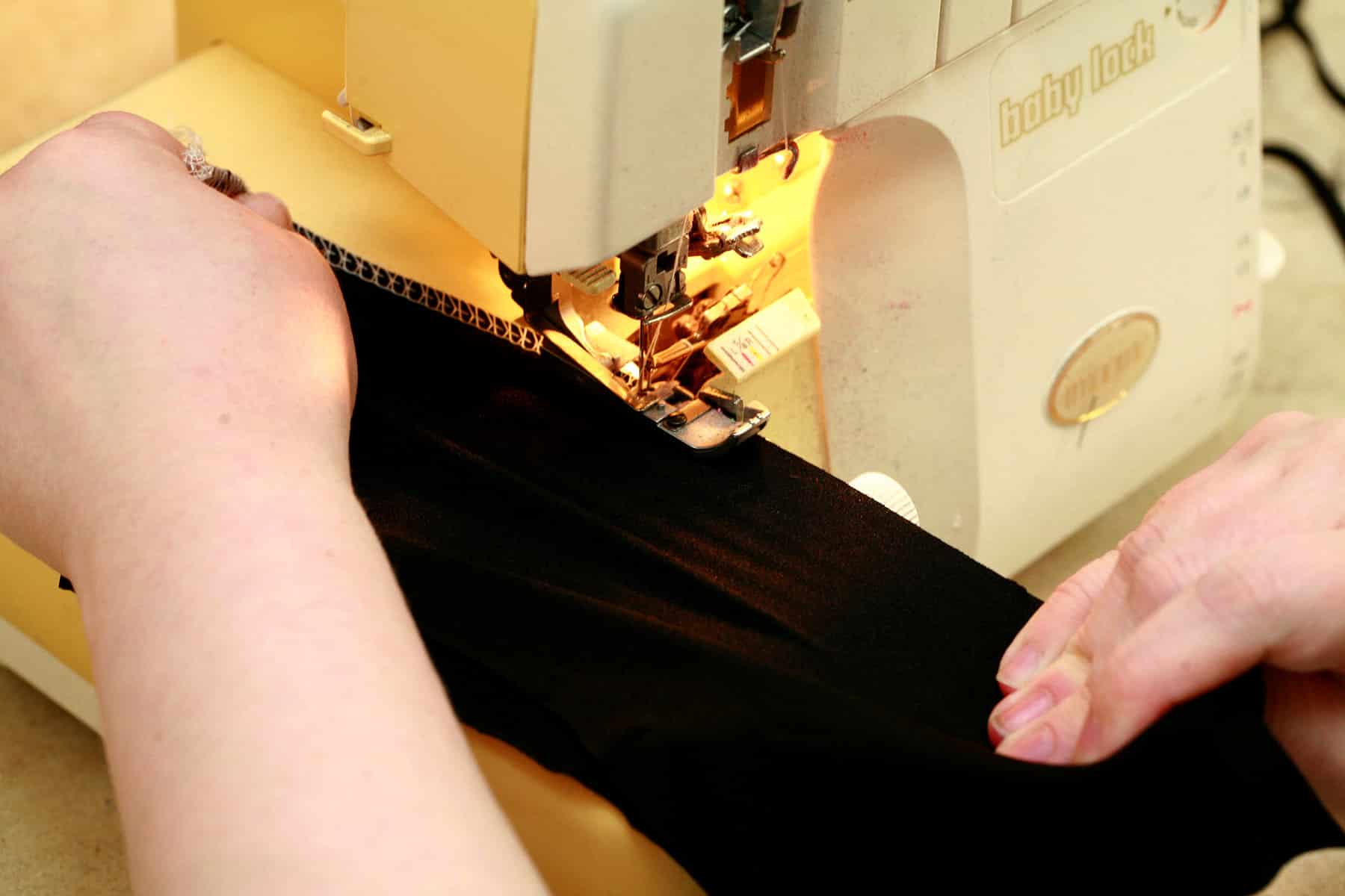 Two hands are sewing spandex with a serger.
