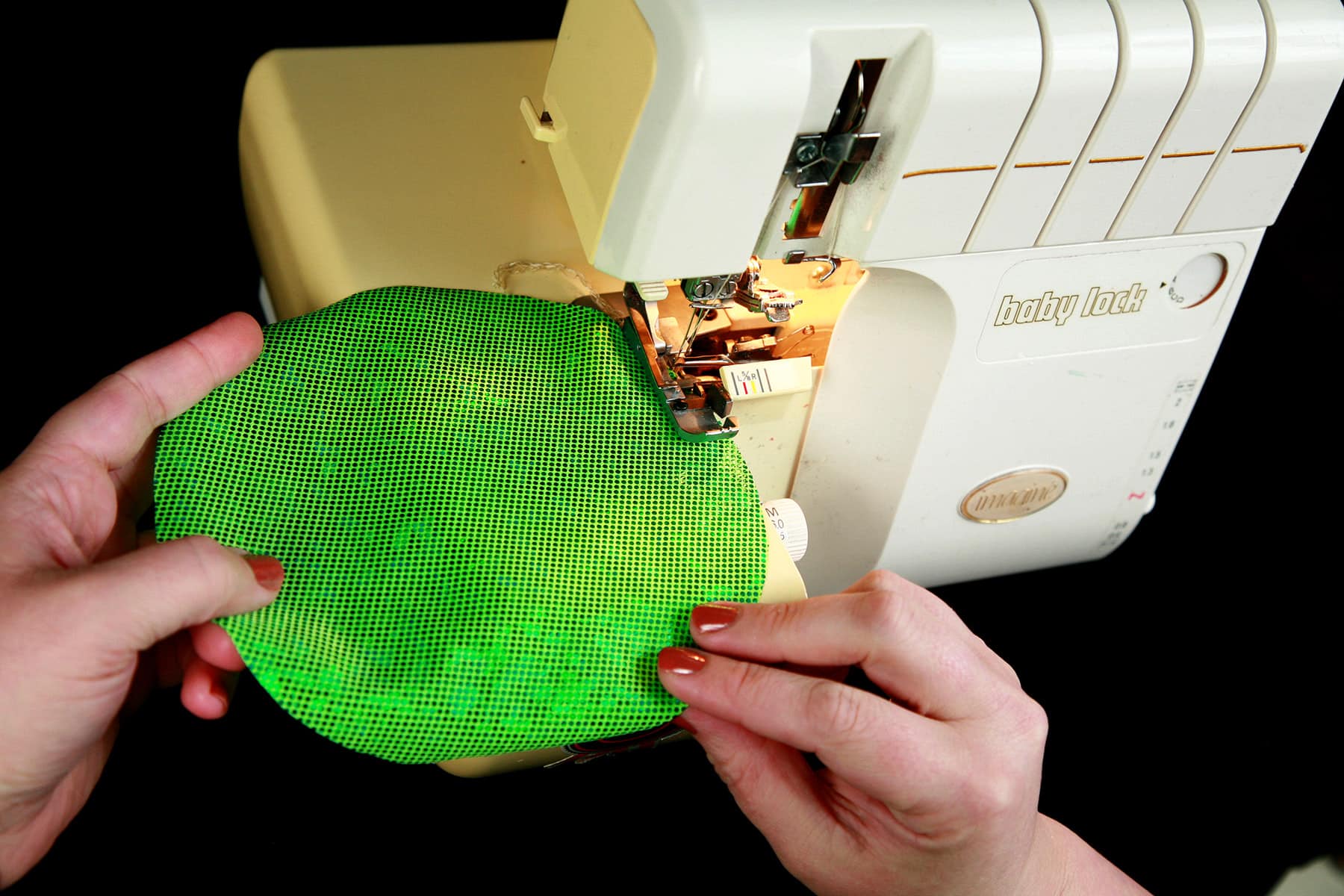 A pair of hands is sewing a bright green circle of fabric.