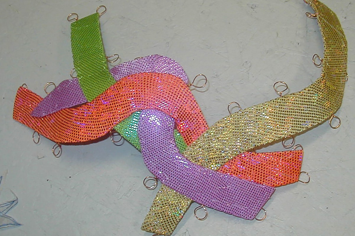 A synchro headpiece, made up of squiggly shapes in 4 colours: lavender, salmon, gold, and lime green.