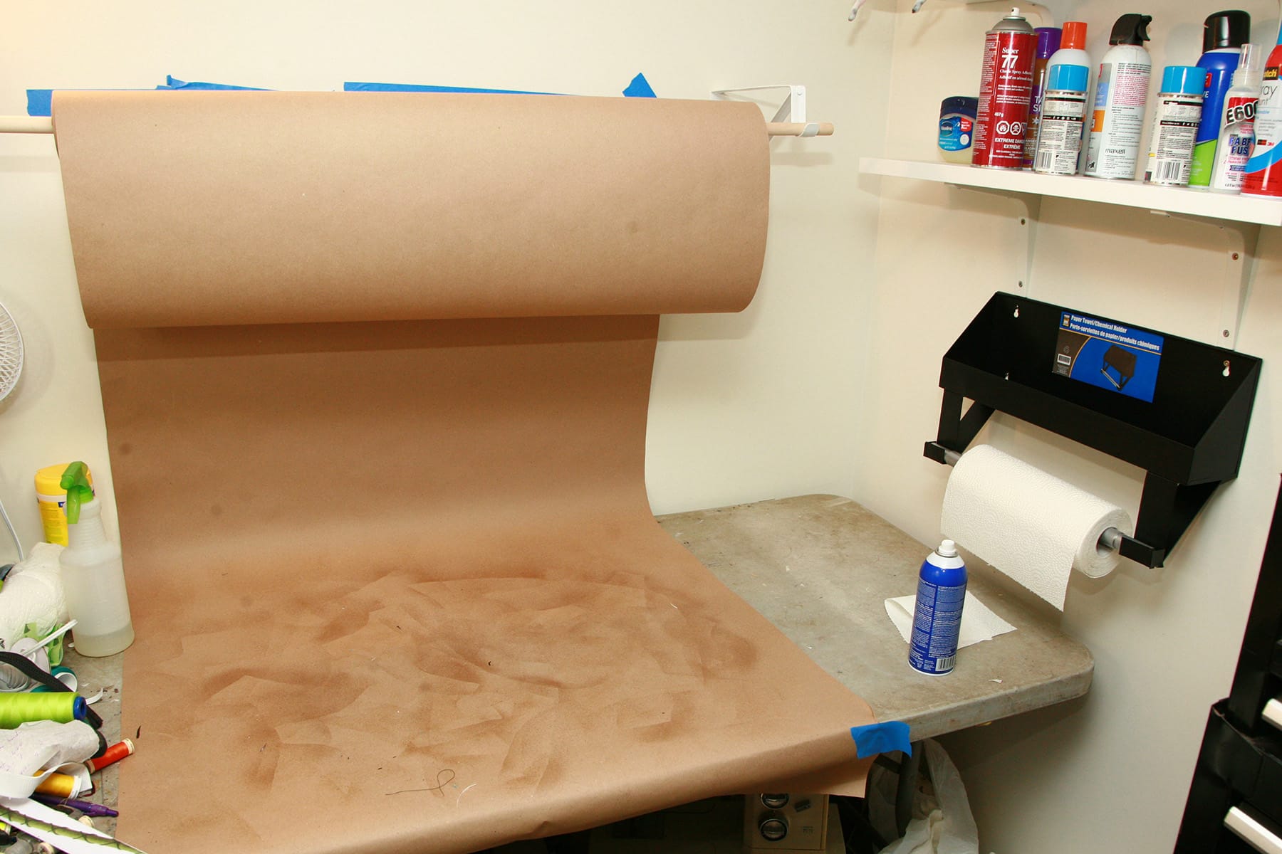 A work table, with a roll of brown craft paper suspended above it. The paper is pulled down and over the table, providing a backdrop for spraying.