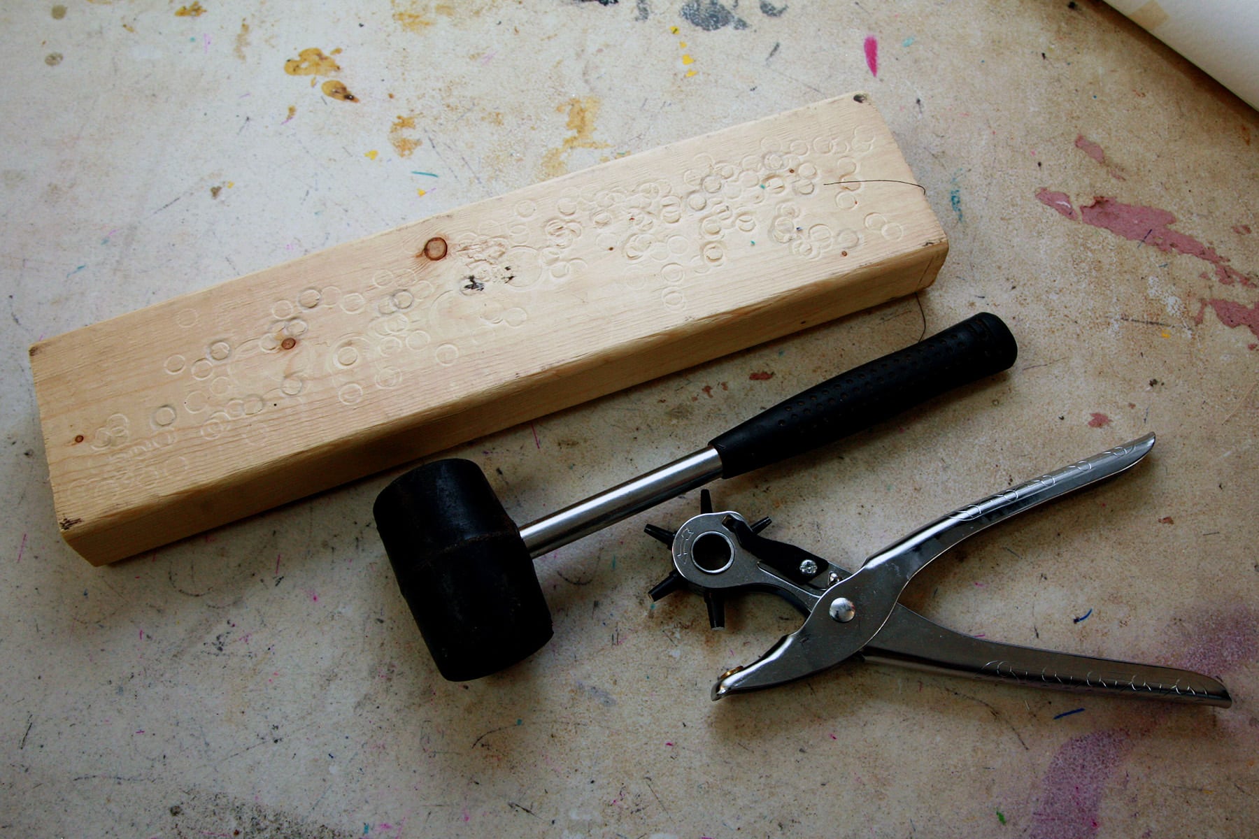 A block of wood, a rubber mallet, and an eyelet punch.