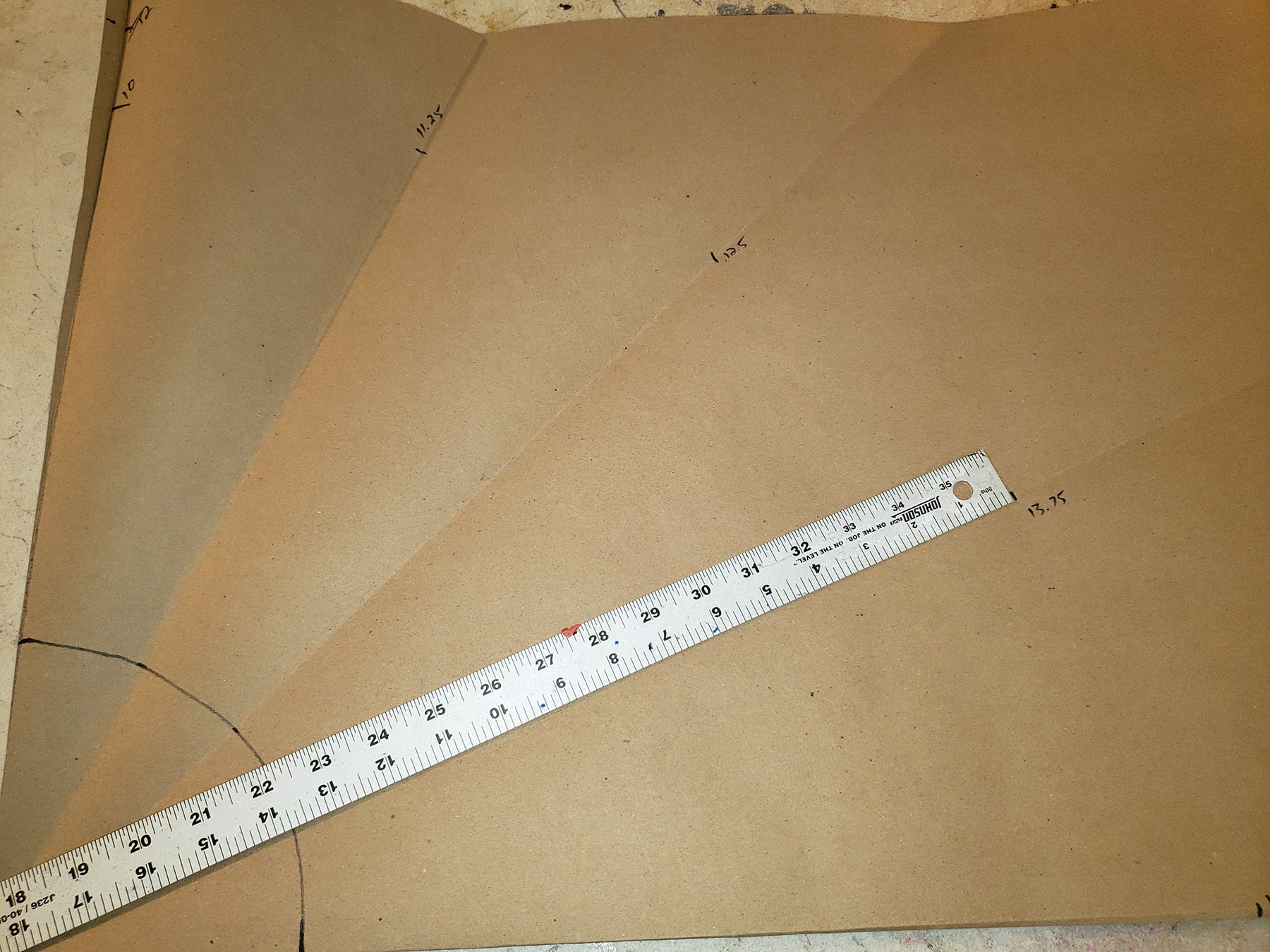 A metal ruler is drafting out a circle skirt pattern on brown craft paper.