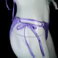 A close up view of the hip of a grey mannequin, wearing a purple bikini.