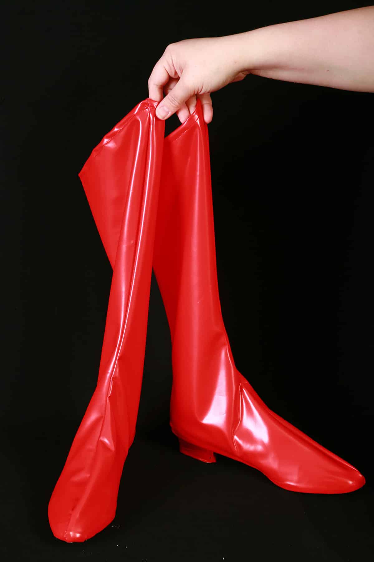 A hand holds up a shiny pair of bright red spandex boot covers.