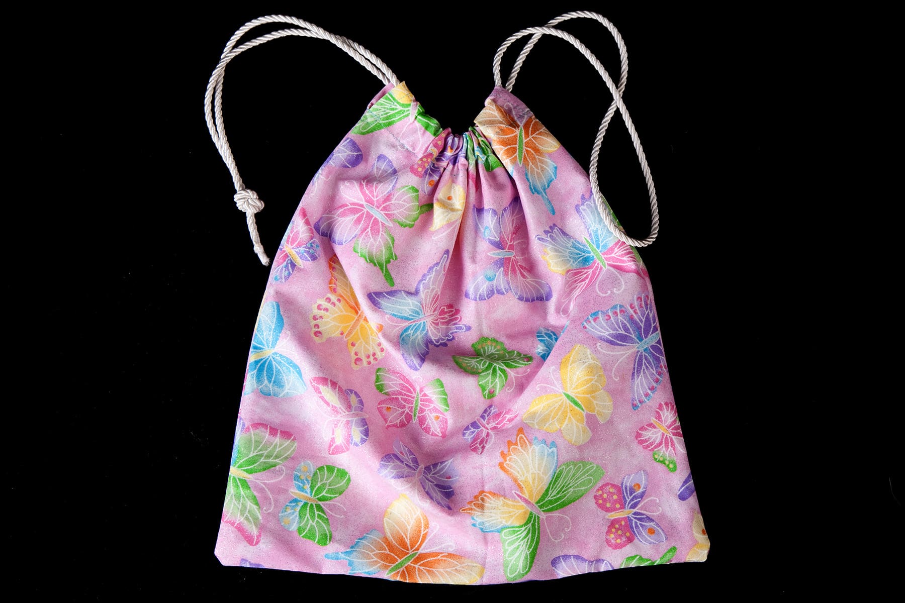 A light purple butterfly print Grip Bag, with a white drawstring cord. It is against a black background.