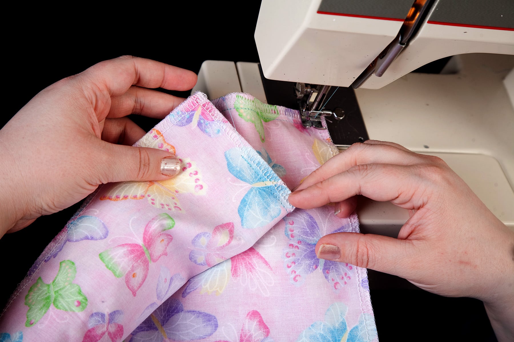 A pair of hands shows a seam on light purple butterfly print fabric.