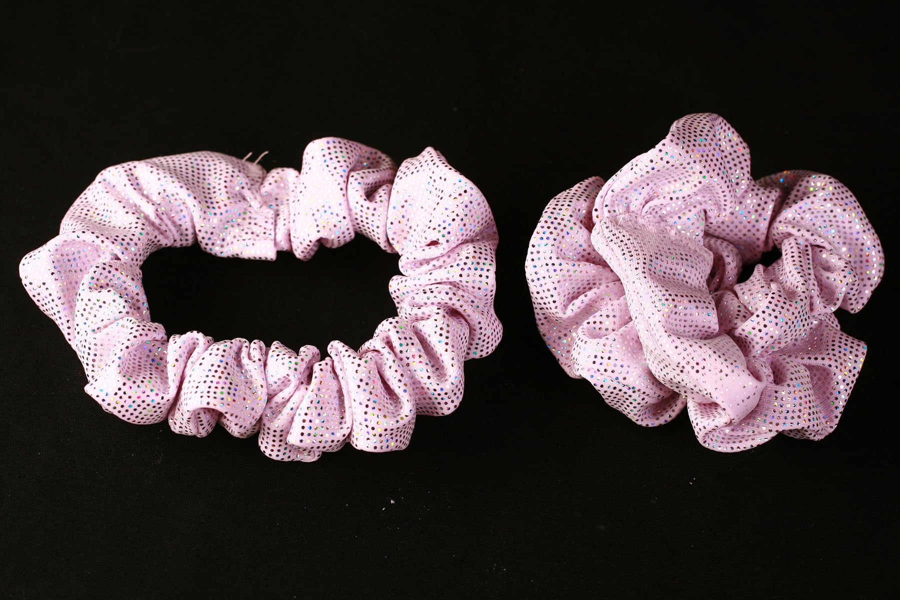 Two sparkling light pink scrunchies are shown against a black background.