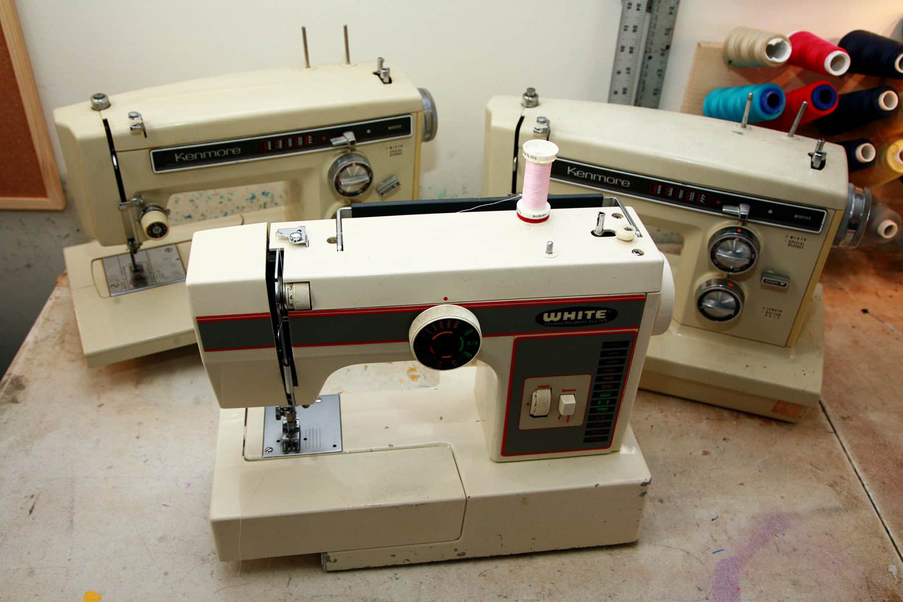 Three older model sewing machines arranged on a work table.