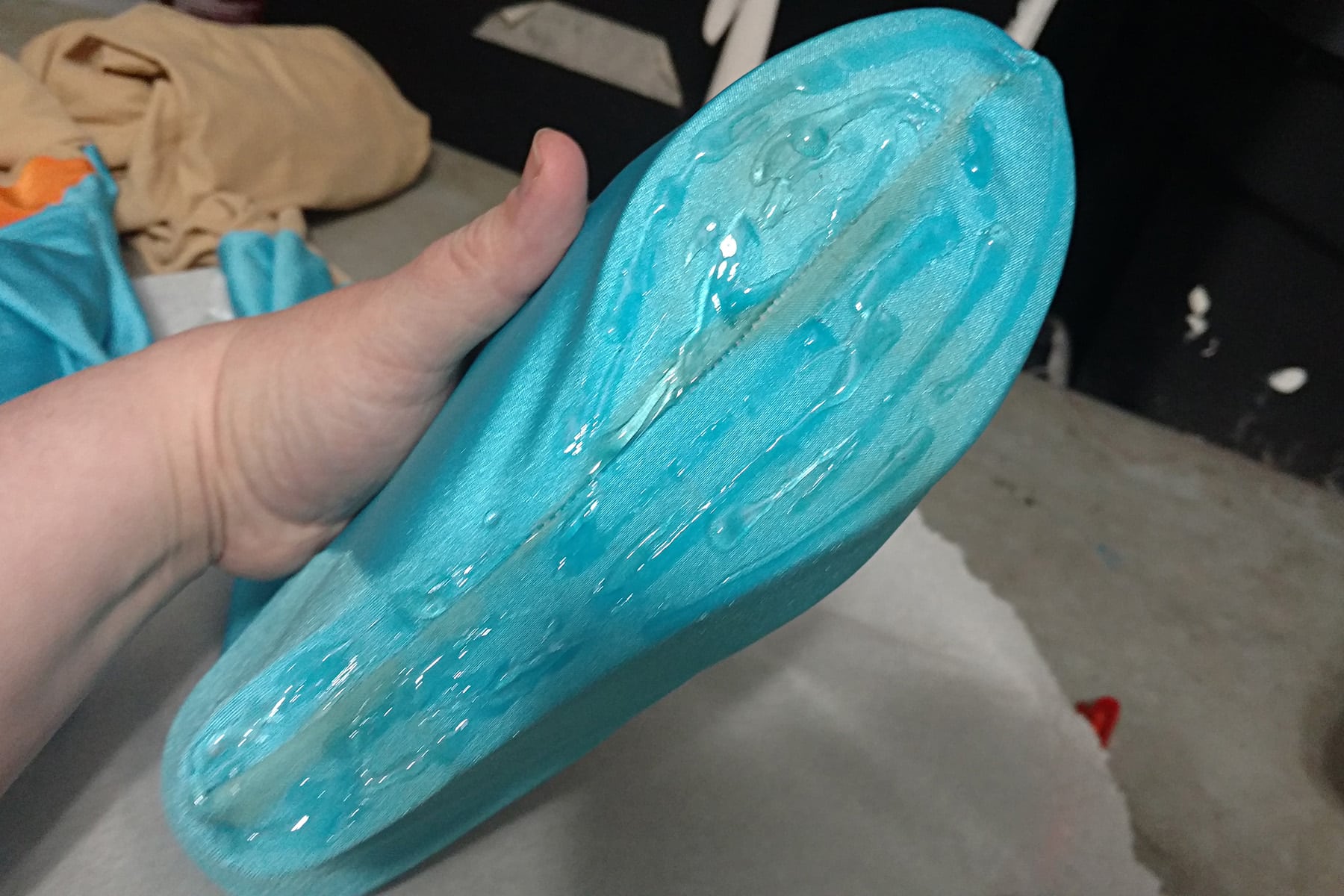 A hand displays the bottom of a blue fabric covered shoe. The bottom is covered in a thick, clear glue.