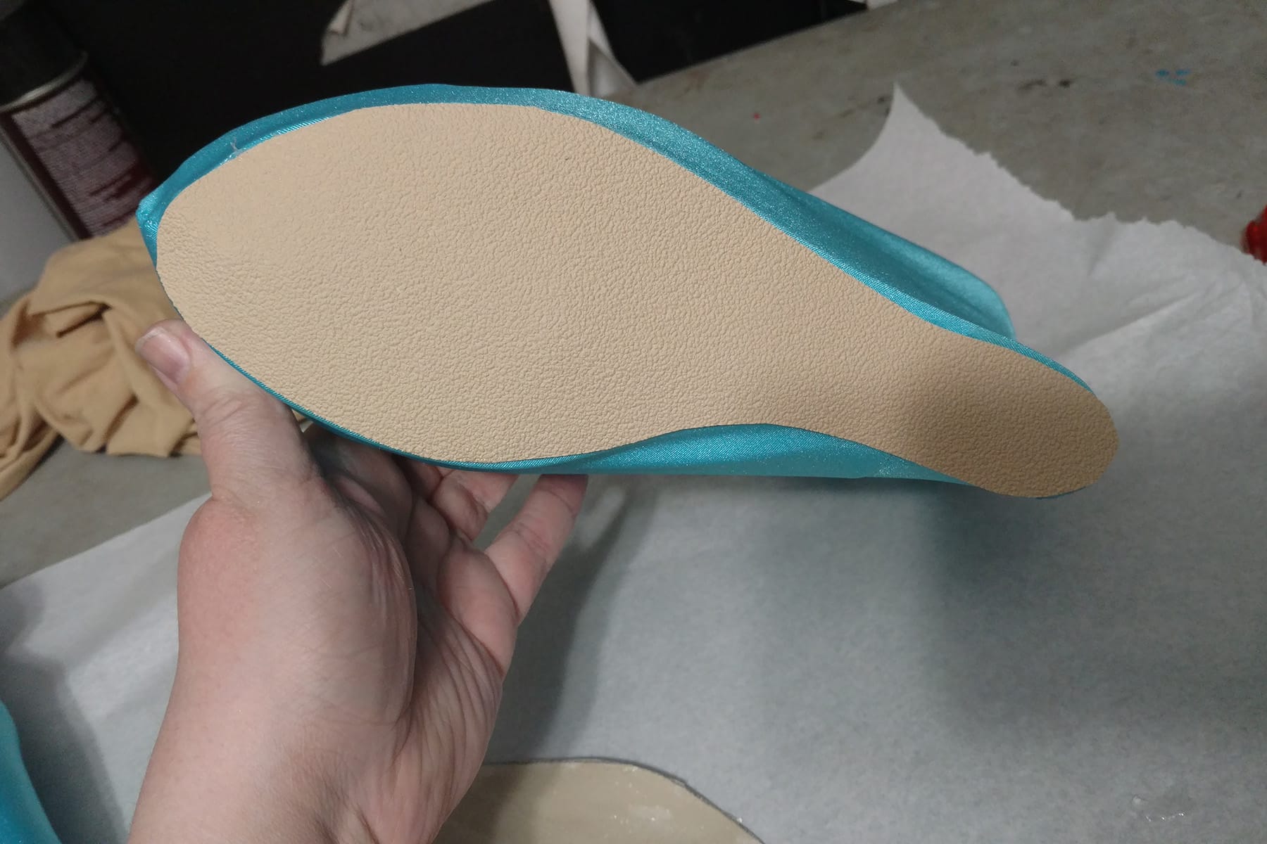 A hand holds a piece of beige coloured nonslip soling fabric against the bottom of a shoe.
