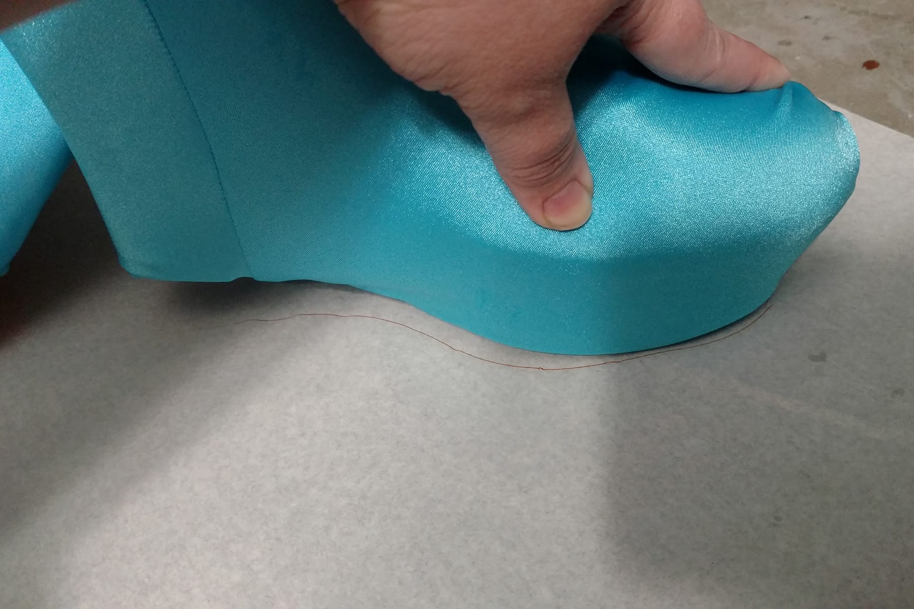 A hand holds a blue, spandex covered shoe flat on a piece of paper.