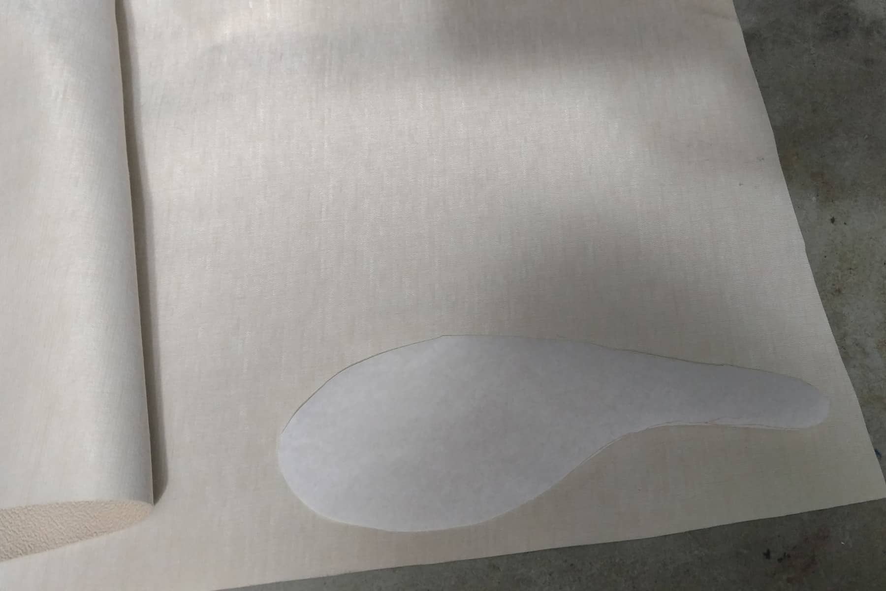 A shoe sole shaped paper pattern is laid against the underside of a piece of soling fabric.