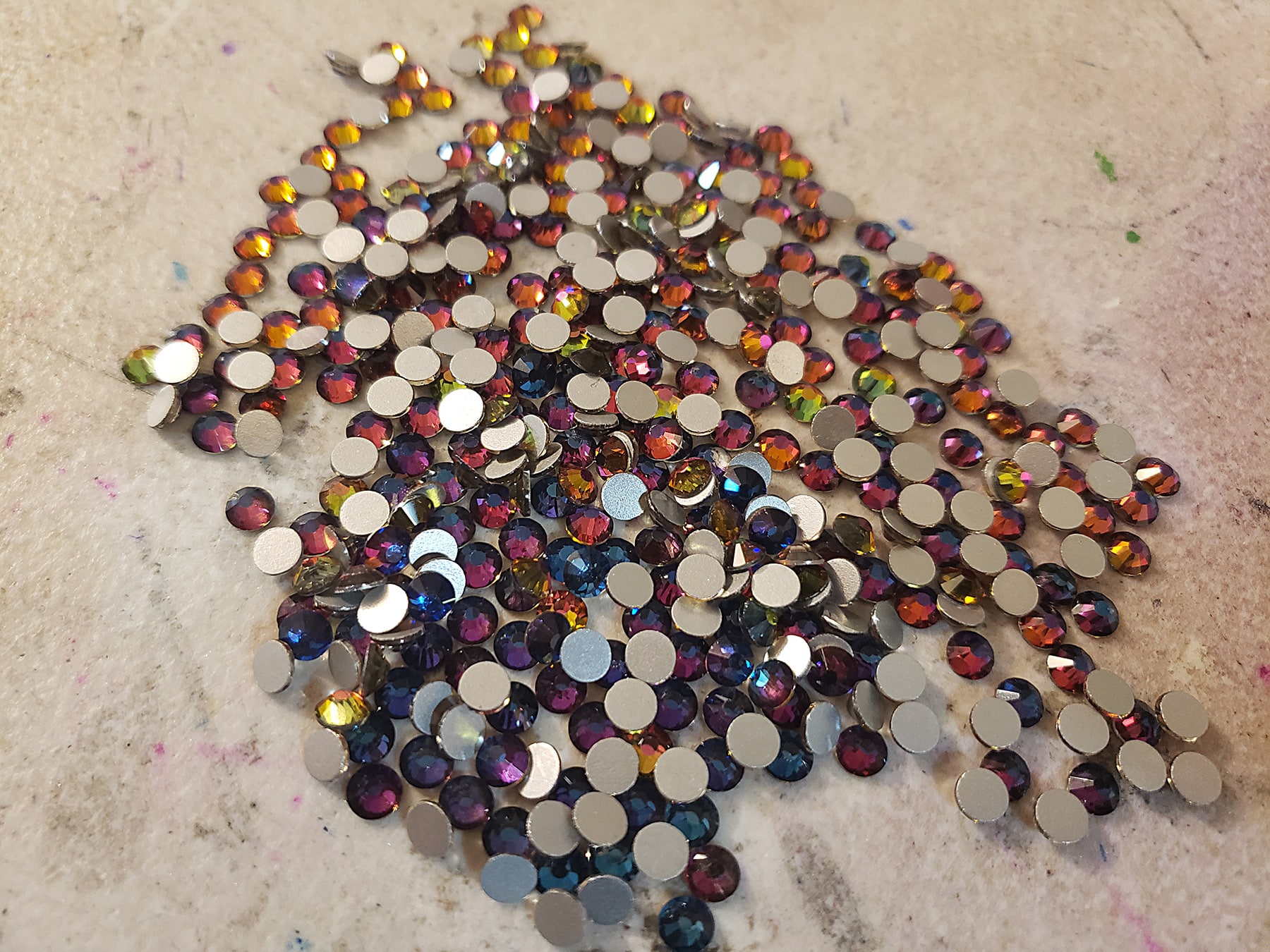 A small pile of purple "volcano" rhinestones. They are purple and blue with pink and orange reflections.