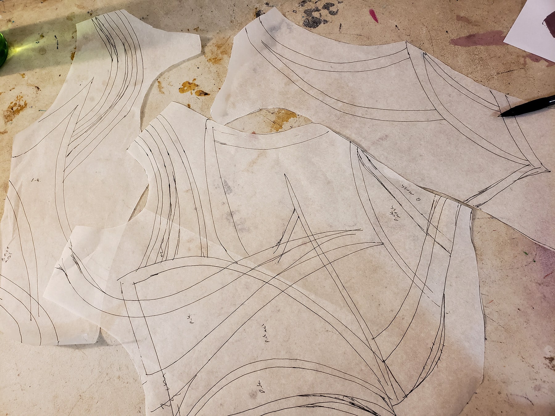 A small pile of bodice pattern pieces on a work table. They are all marked with design lines.