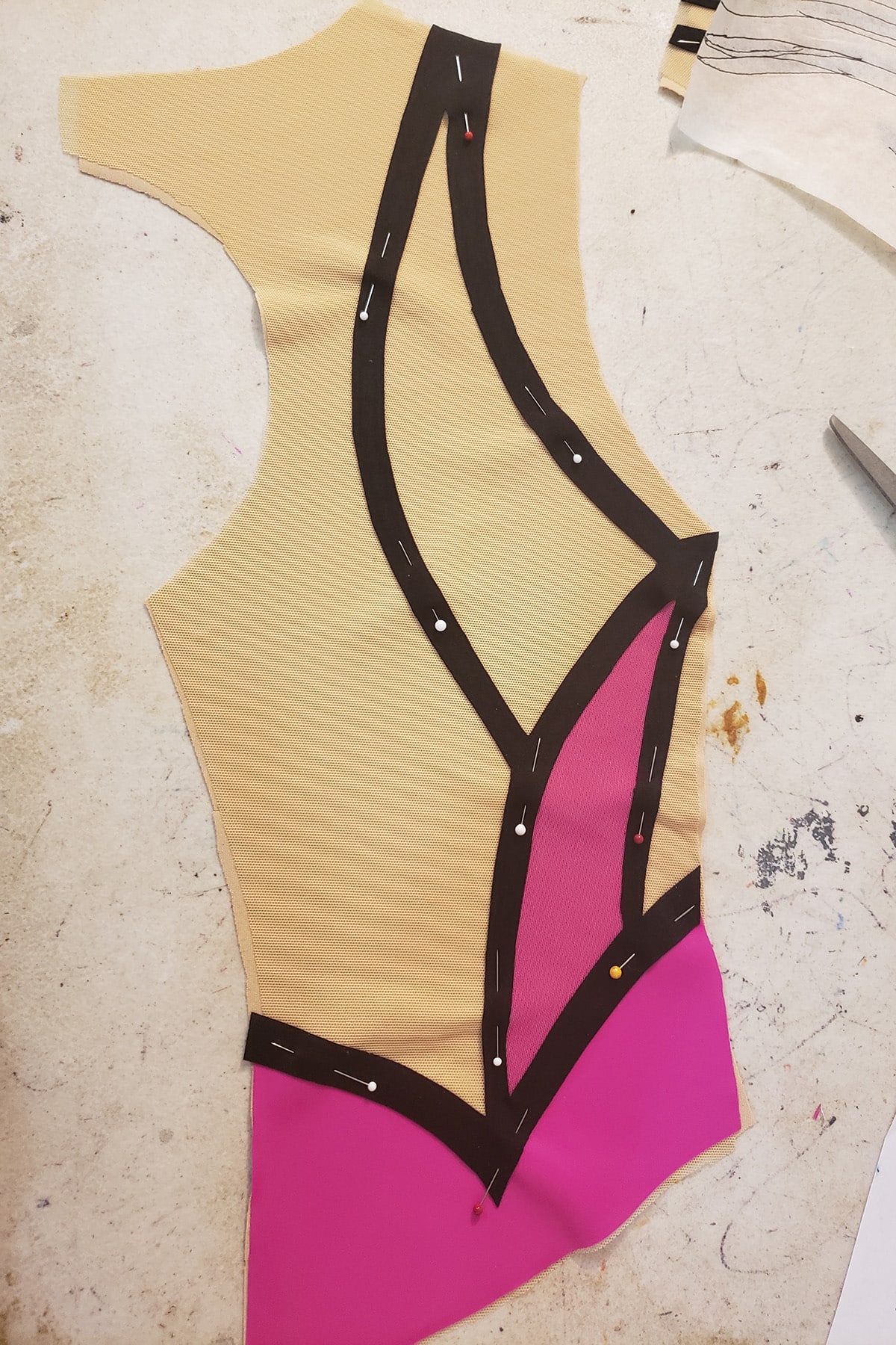 The right back half of the bodice, pinned together. It is a beige fabric piece, with pink and black pieces of fabric pinned to it.