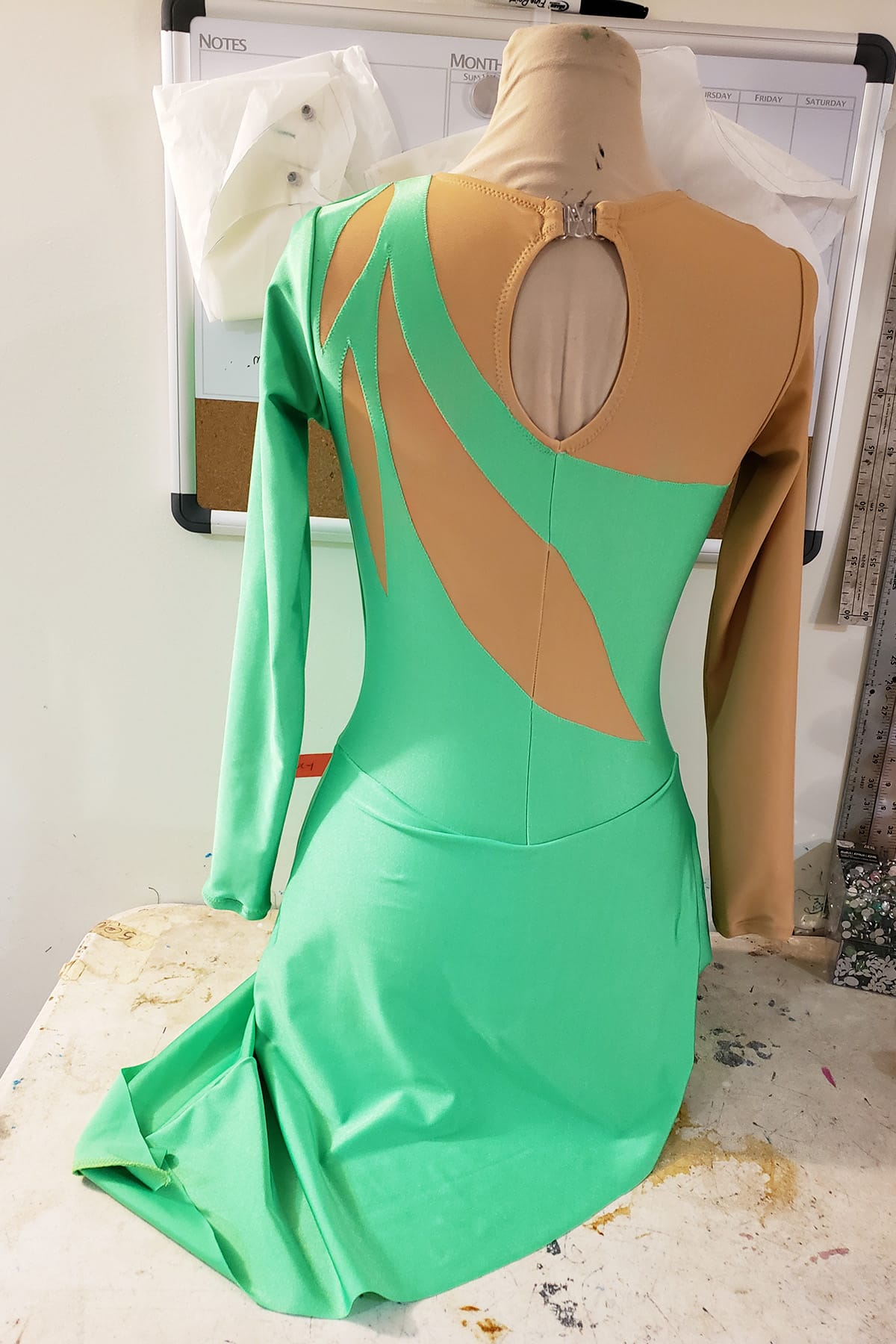 Back view of a basic green figure skating dress on a dress form.