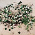 A pile of clear and green rhinestones, on a grey work surface.