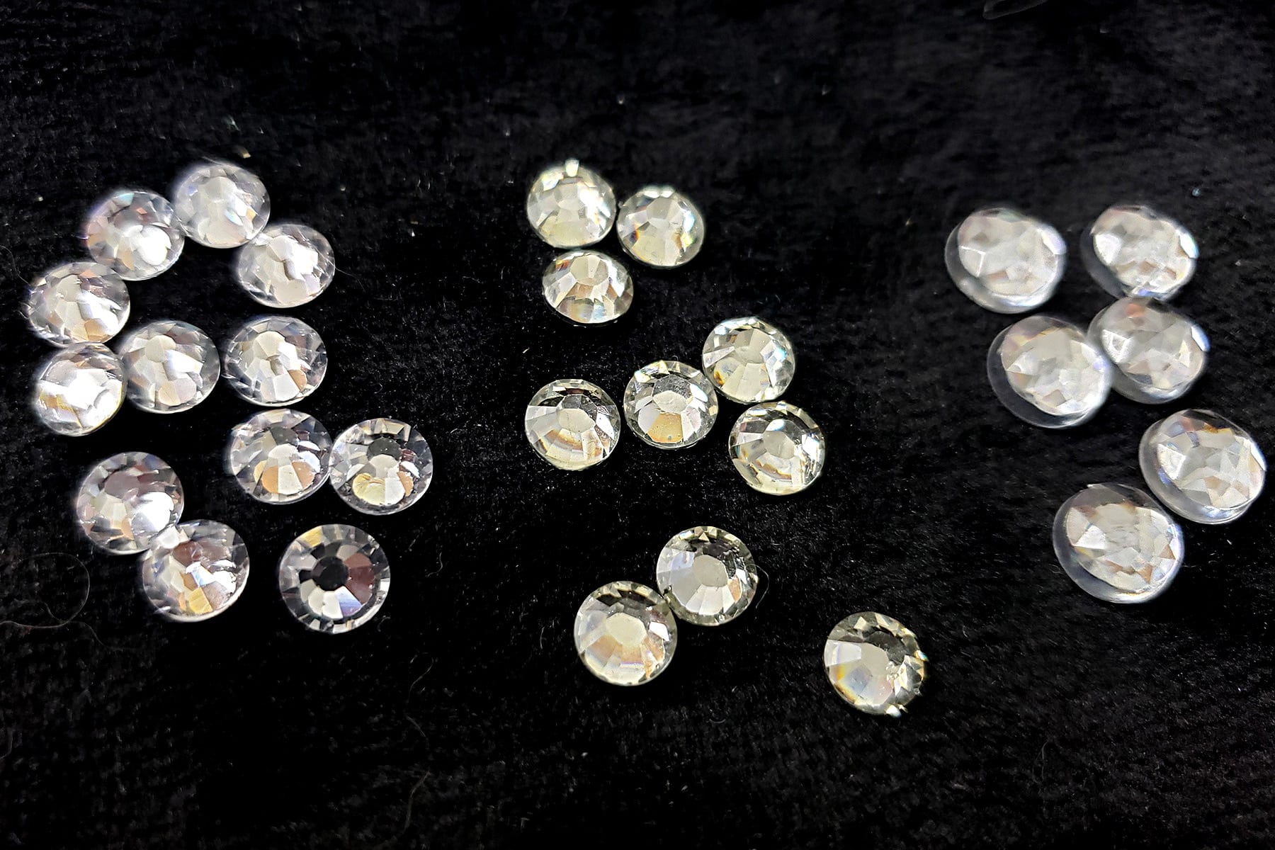 A side by side comparison of 3 small piles of clear rhinestones.