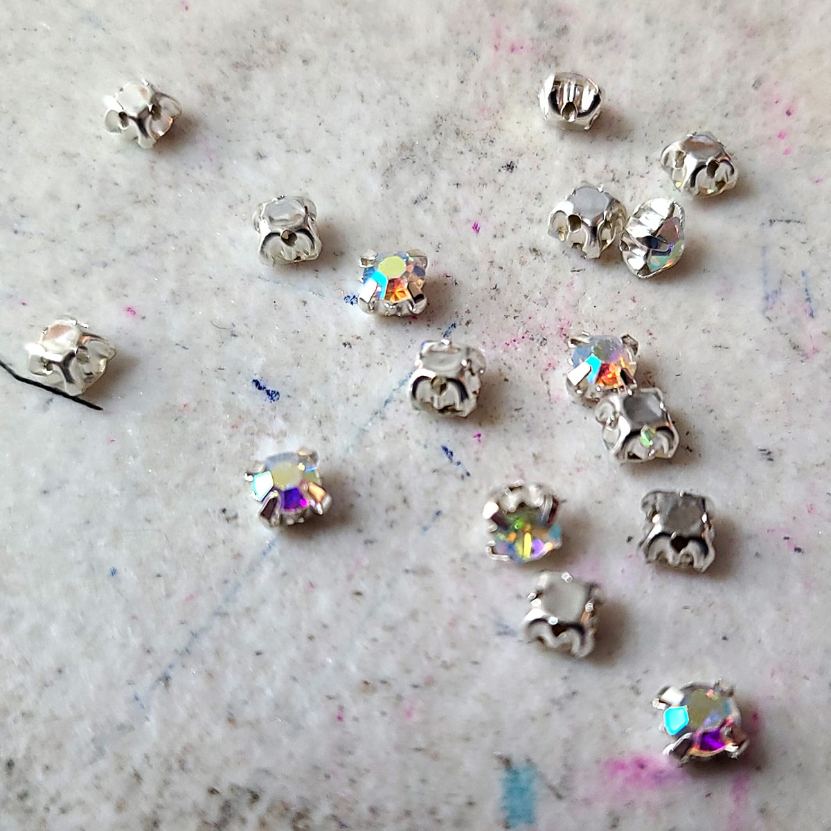 A small handful of round rhinestones in silver coloured prong settings, scattered on a grey work surface.
