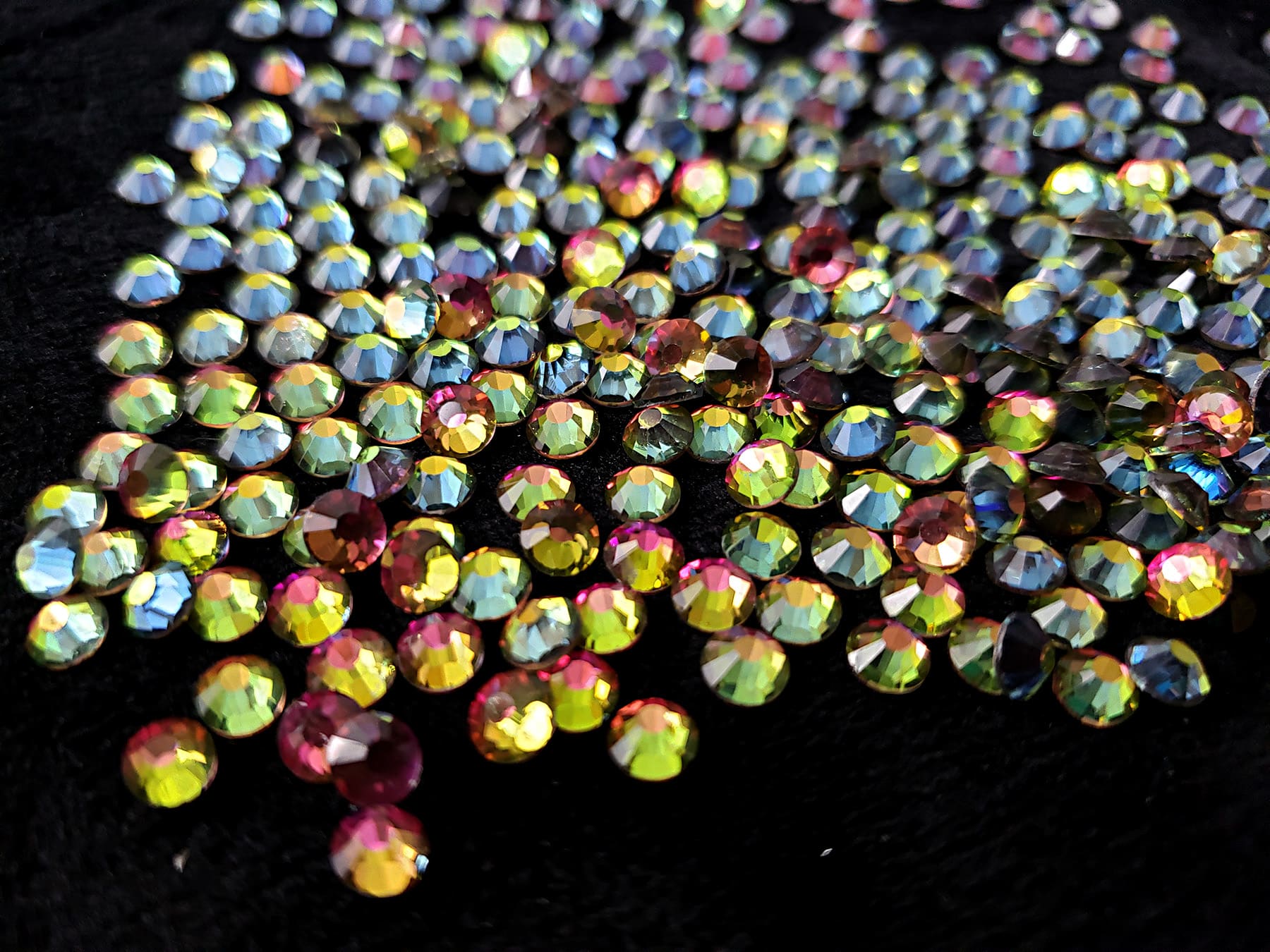 A large pile of iridescent rhinestones against a black background.