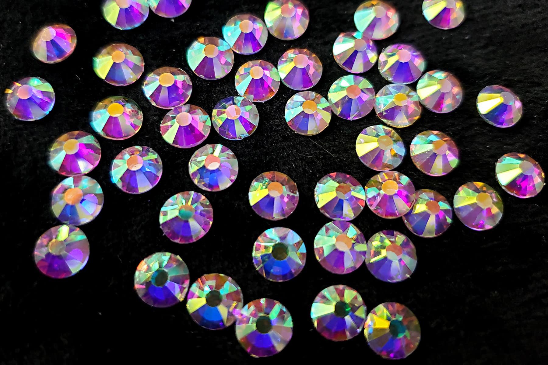 A large pile of iridescent rhinestones against a black background.