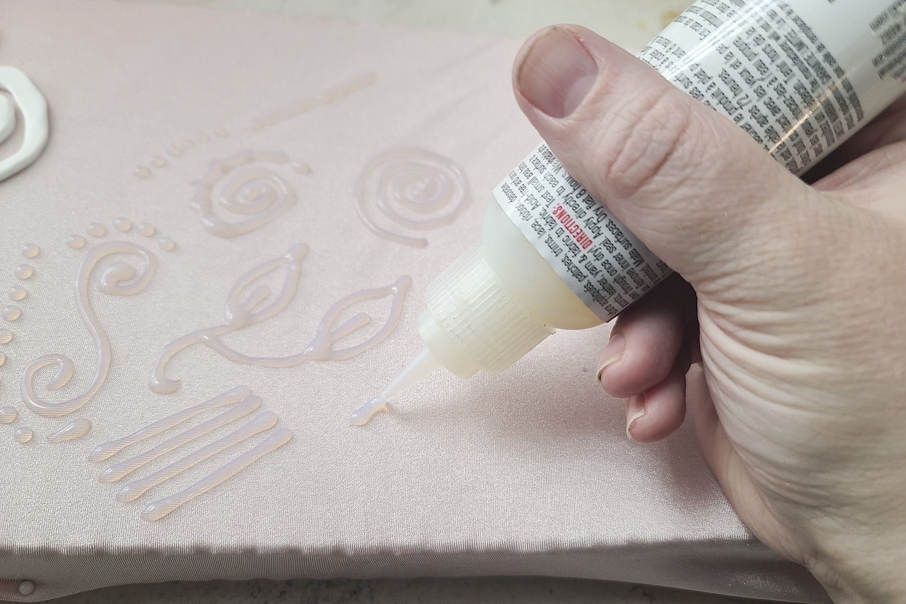 A tube of E-6000 fabri-fuse is being used to pipe designs on pale pink spandex.