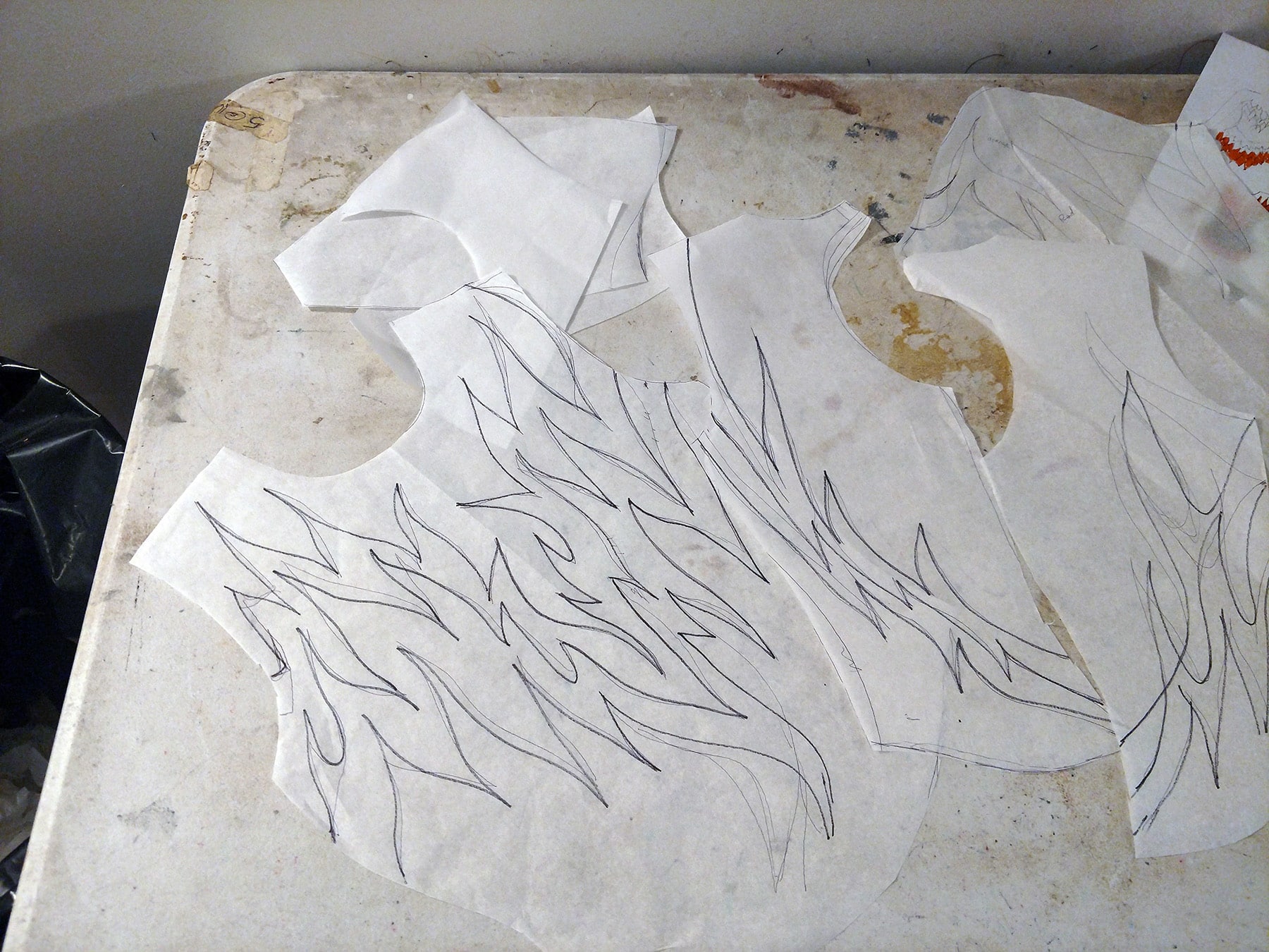 Several white paper pattern pieces on a work surface, all marked with a flames design.