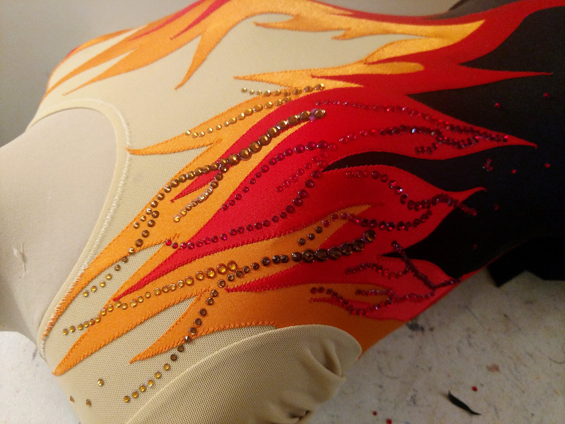 A close up view of the flames dress on a dress form, with red and orange crystals applied to it.