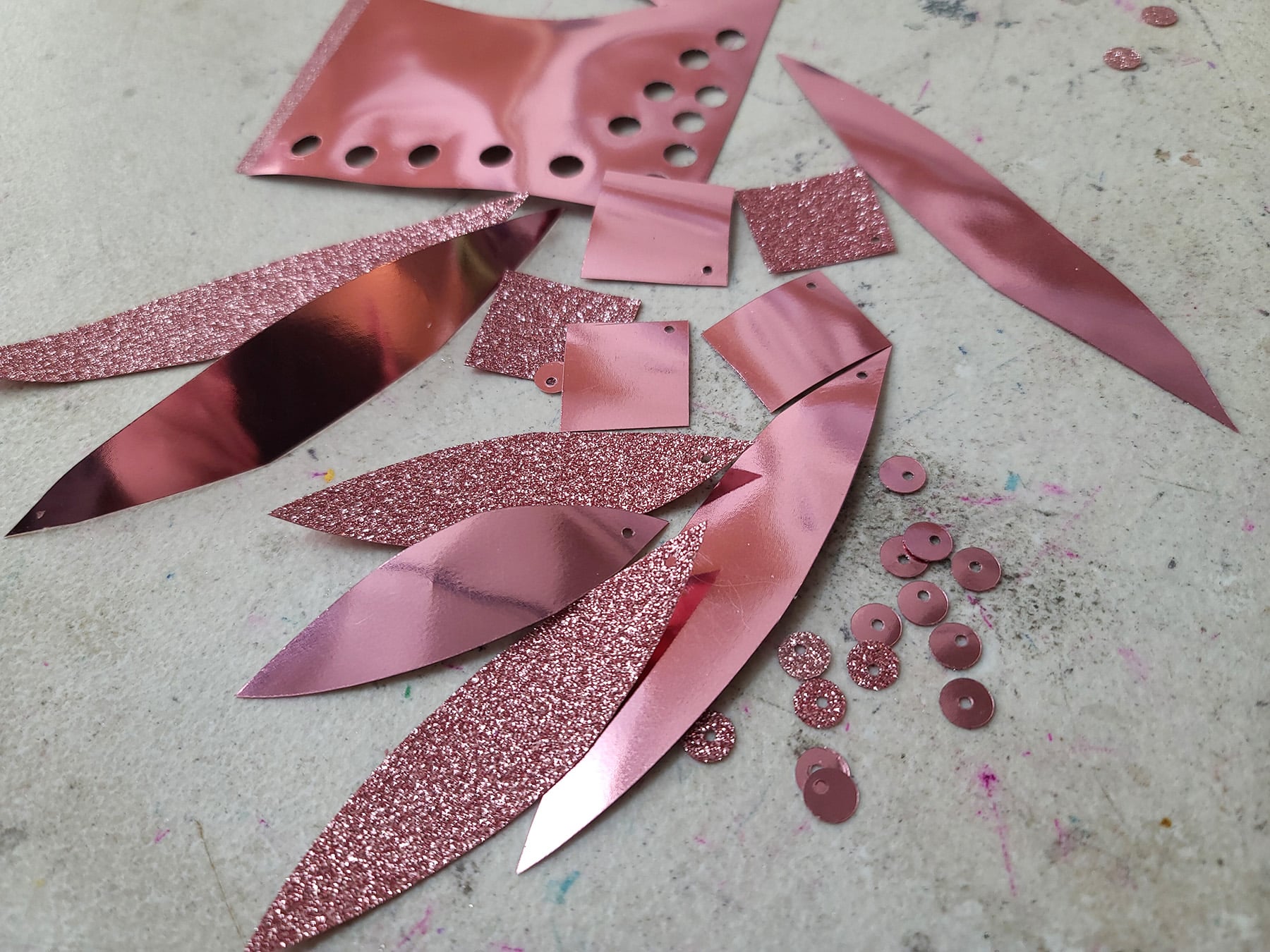 A small pile of pink metallic and pink glitter homemade sequins, made from this How to Make Sequins Tutorial.