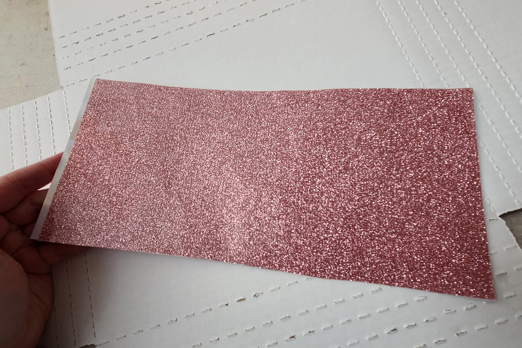 A hand holds a long rectangular piece of pink glitter vinyl.