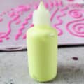 A small squeeze bottle of neon yellow stretch fabric paint in front of a piece of light pink fabric with dark pink fabric paint swirls all over it.
