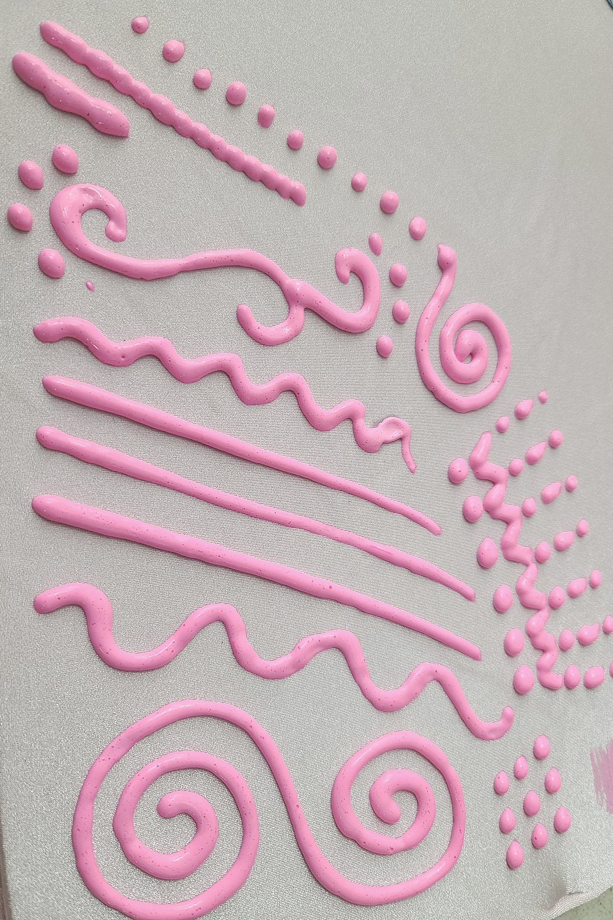 Various lines, squiggles, and swirls of neon pink stretch paint on a piece of light pink spandex.