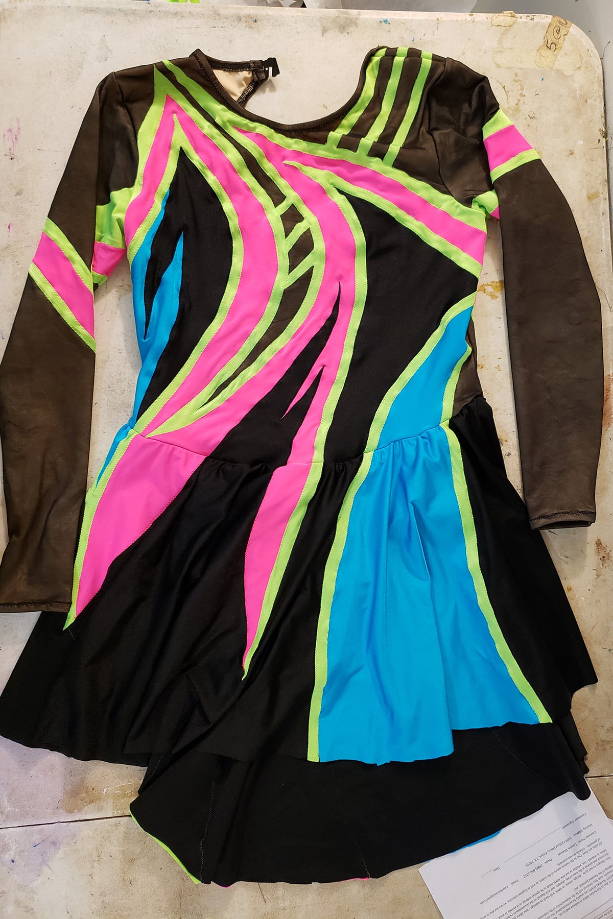 A front view of the 80's themed figure skating dress. It is black spandex and black mesh, with swirls of neon pink, lime green, and sky blue on it.