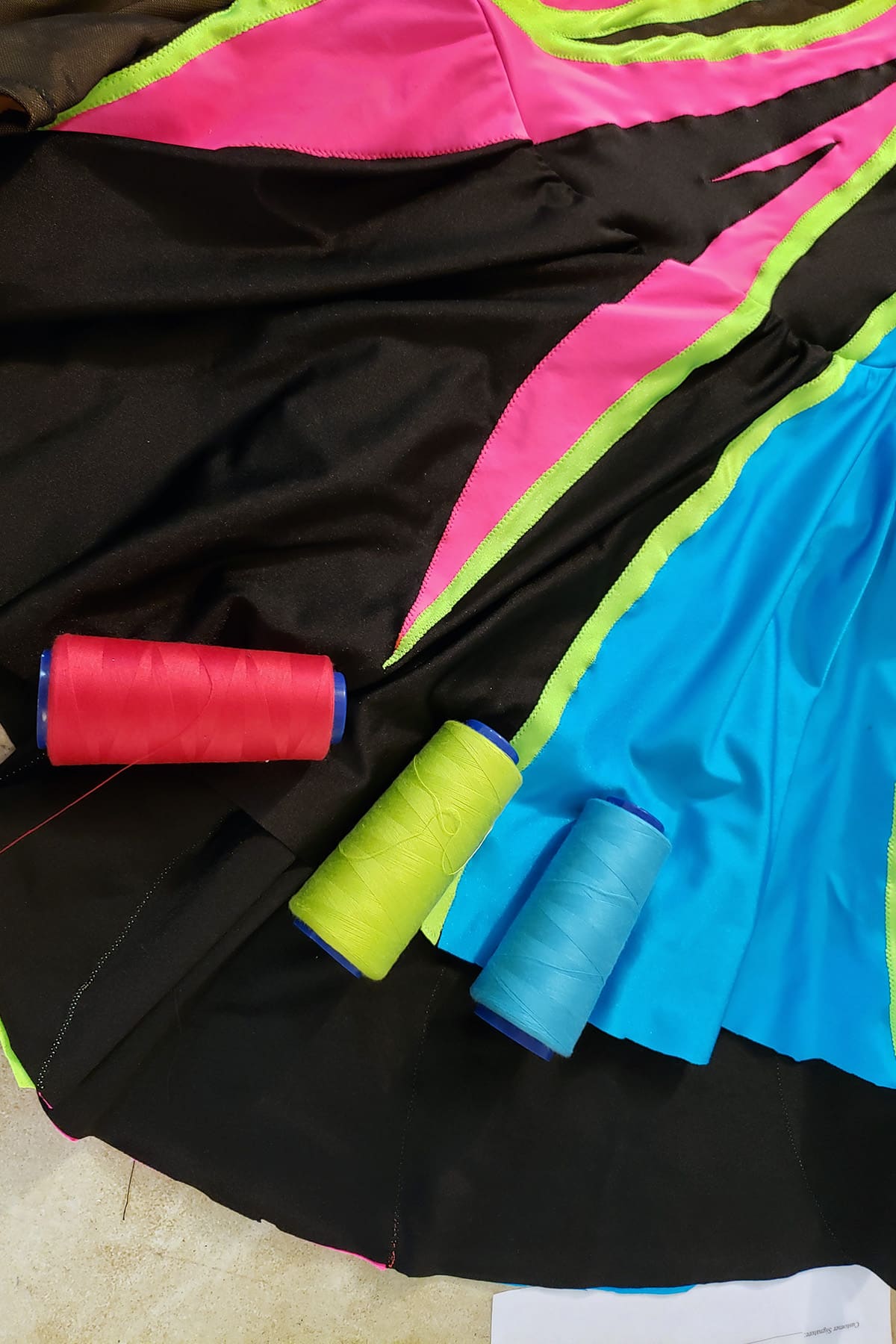 3 large serger cones of thread in pink, lime green, and sky blue are resting on the skirt section of this skating dress.