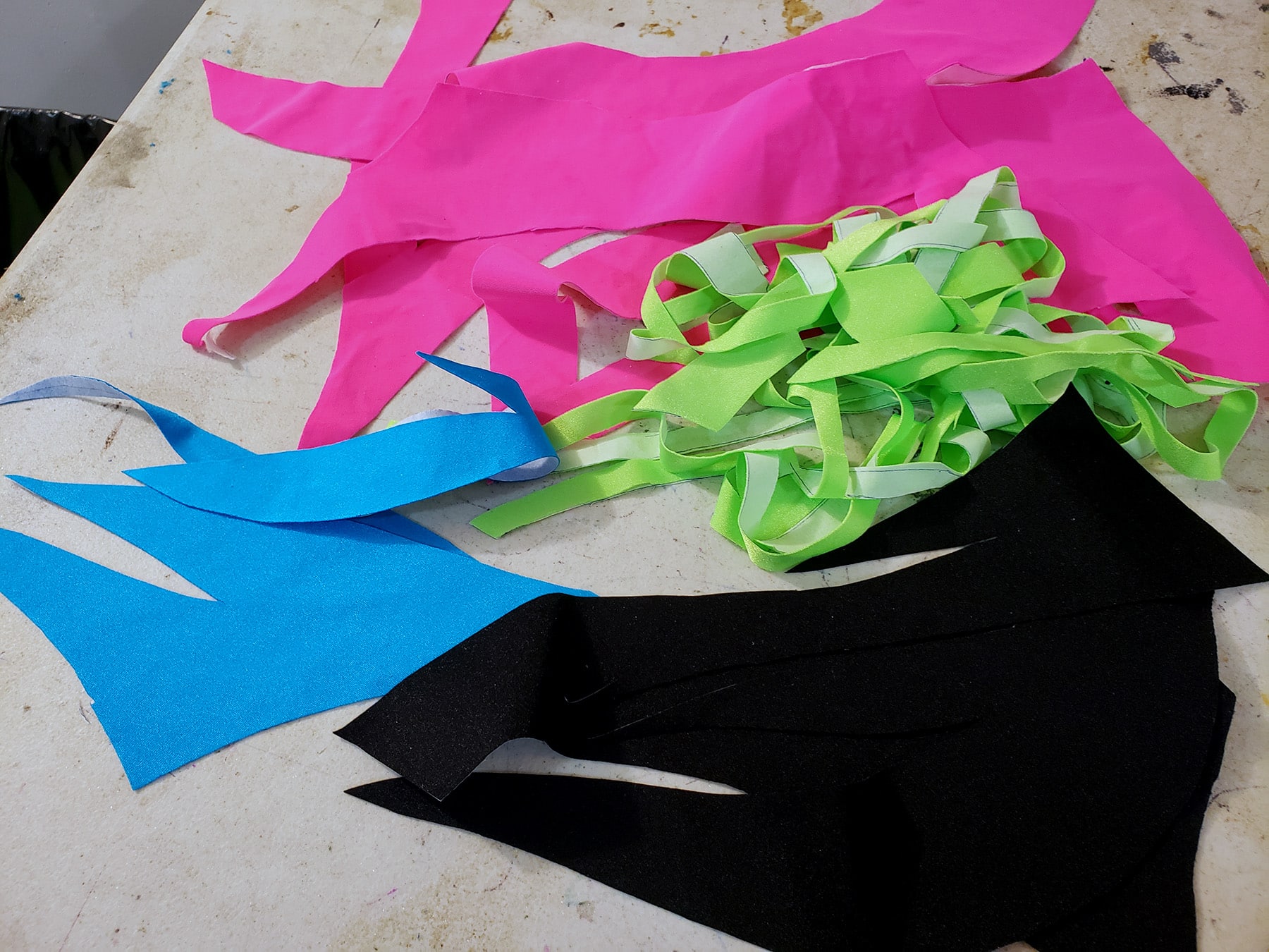 Small piles of bright cut spandex pieces in neon green, neon pink, sky blue, and black.