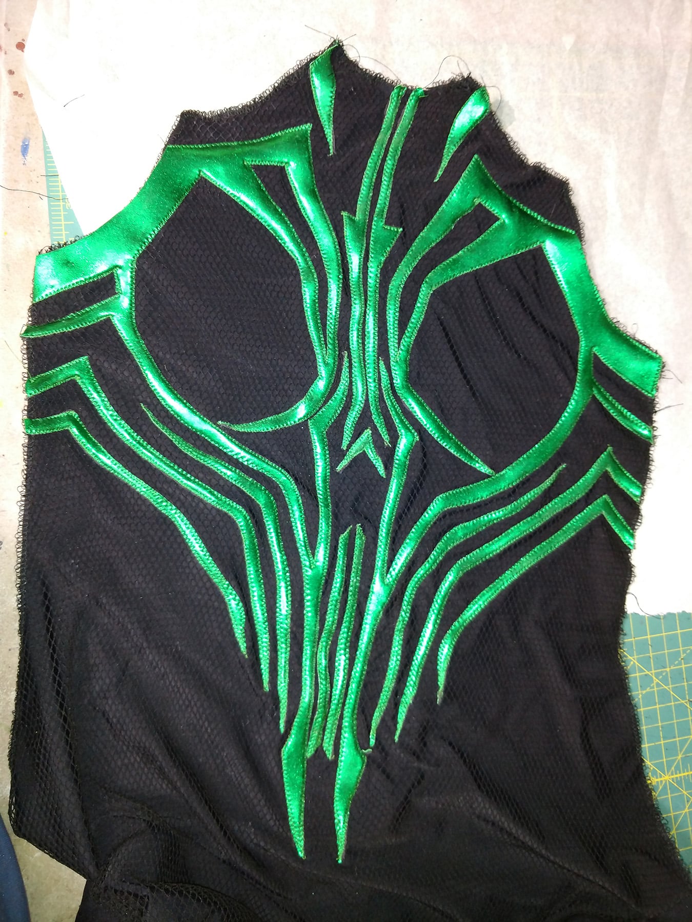 An intricate design of shiny green spandex, stitched down in place on a piece of textured black spandex.