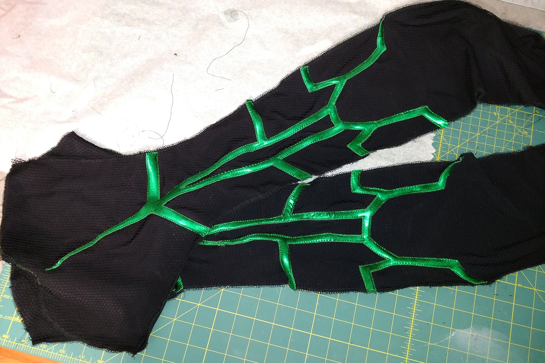 An intricate design of shiny green spandex, stitched down in place on a piece of textured black spandex.