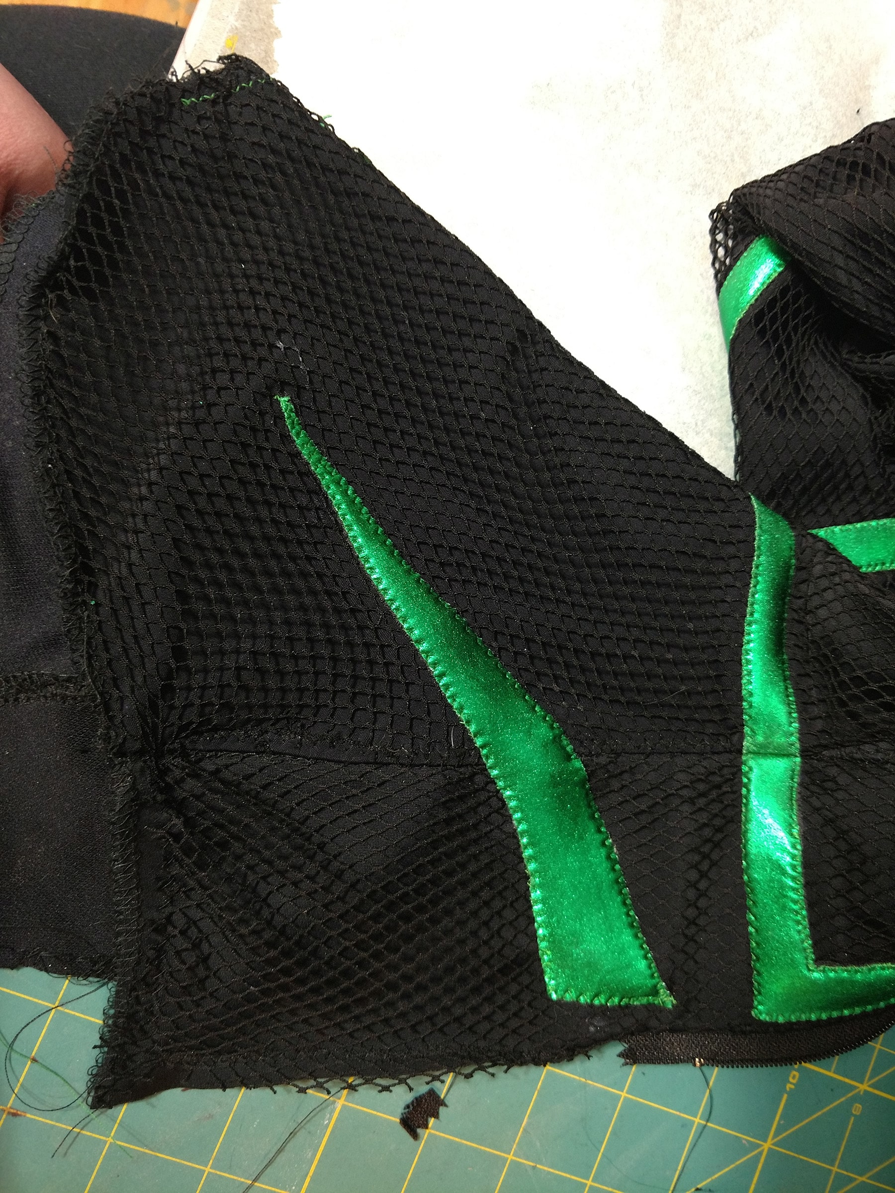 A close up view of a black spandex "foot" part of the costume, with two pieces of shiny green spandex stitched across it.