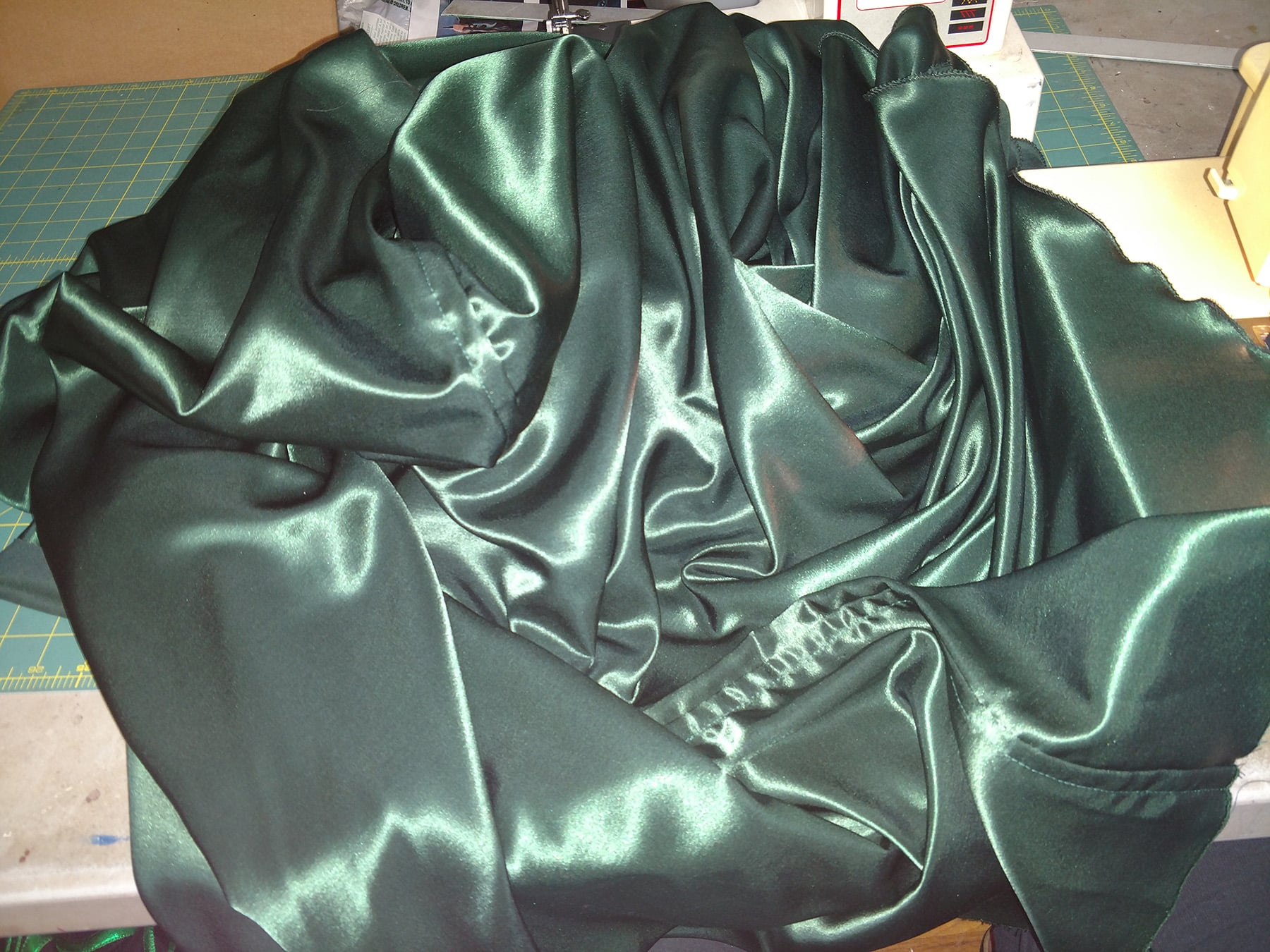 A large green satin cape is bunched up at a sewing machine.