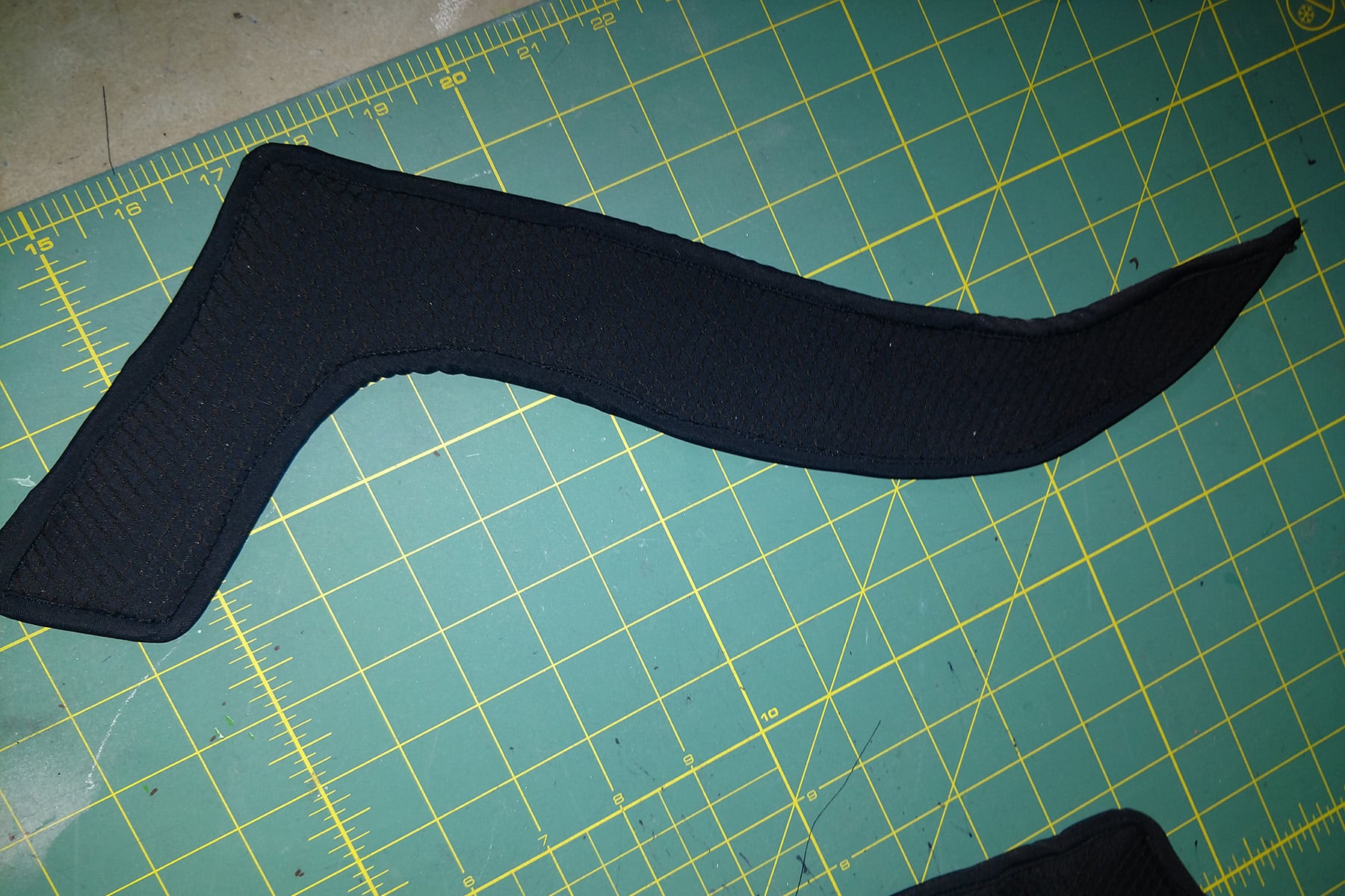 A vaguely "L" shaped cruved piece of textured black spandex, laid out on a green work surface.