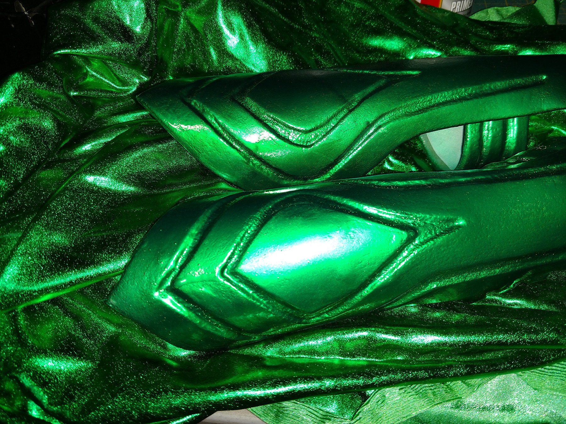 A pair of metallic green Hela bracers are shown against a pile of matching metallic green spandex.