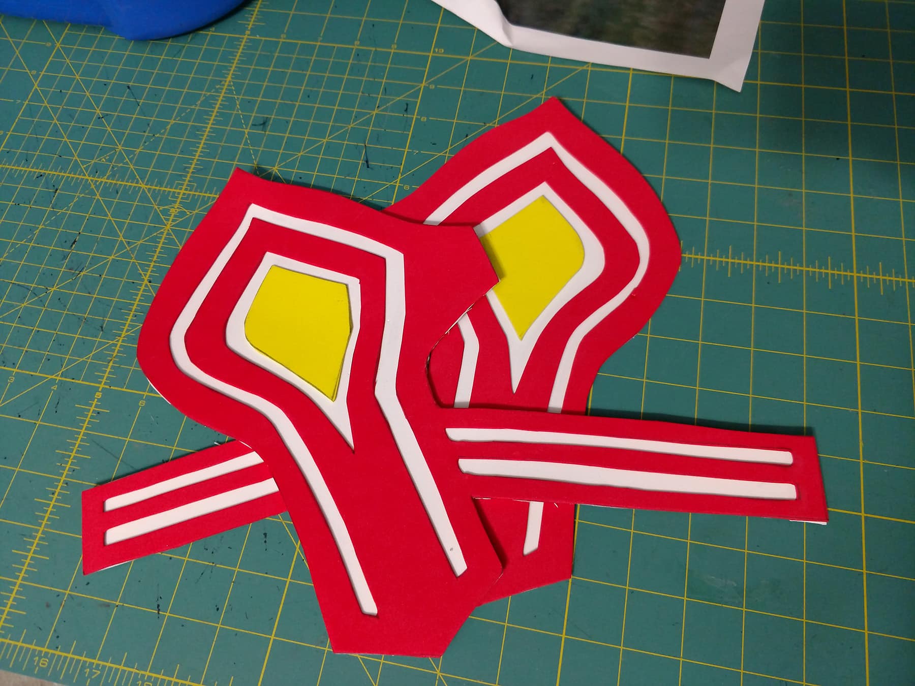 Two bas e bracers made from craft foam. Red and yellow design pieces have been glued down onto a white base piece.