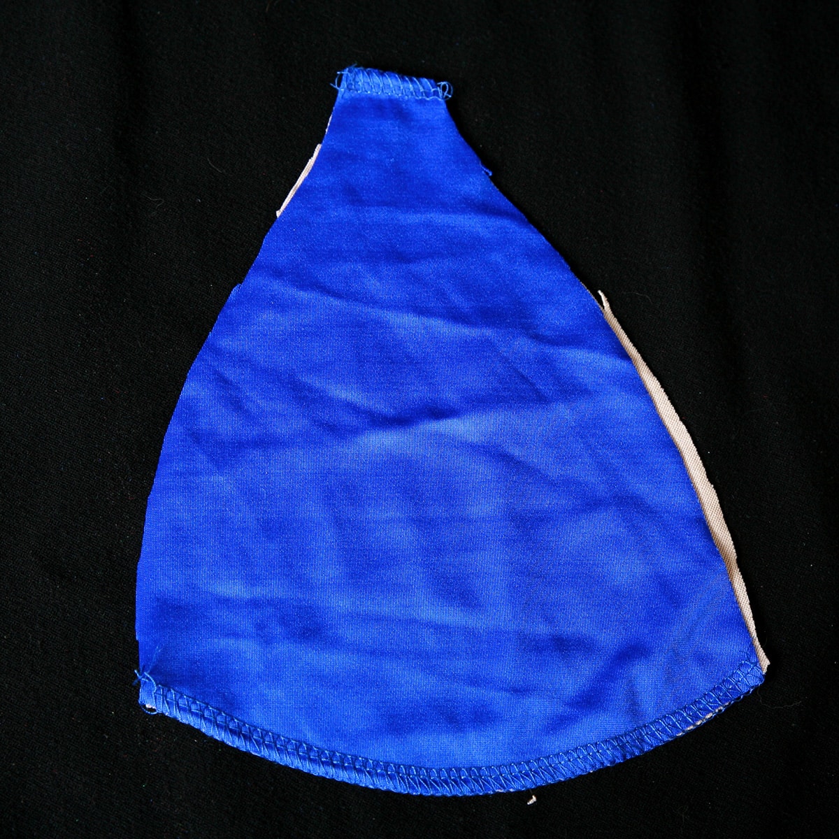 A curved triangle shape of blue spandex rests on top of a piece of beige lining in the same shape. They are sewn together at the top and bottom edges.