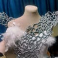 A close up view of the top of the front bodice of the wedding gown, on a dress form. Both wings are attached to the gown.