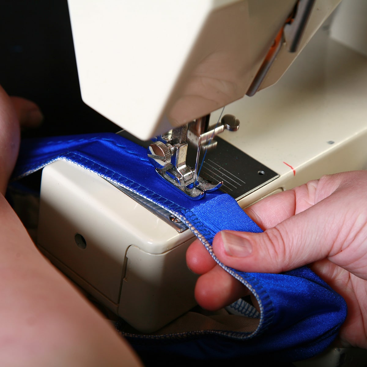 A blue bikini bottom being guided through a sewing machine.