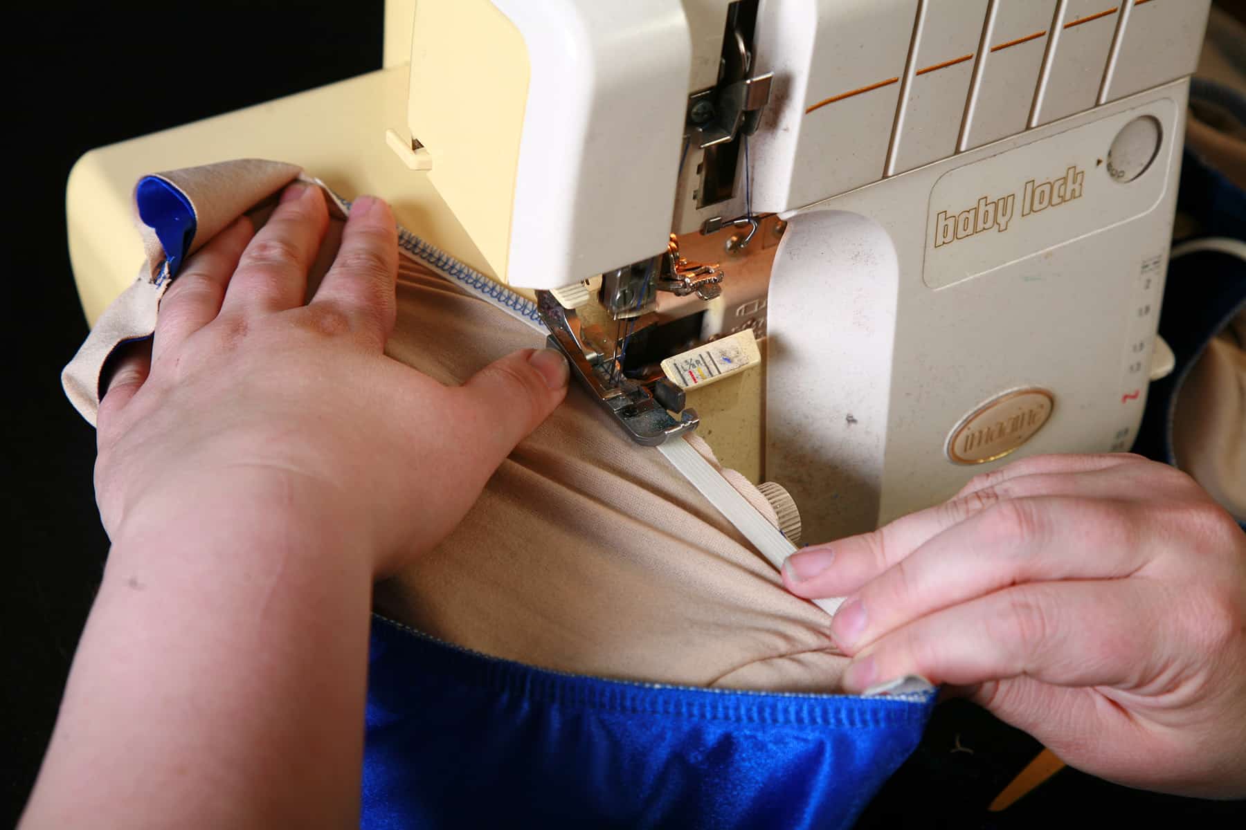 Hands guide a blue, lined bikini bottom through a sewing machine.